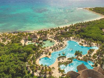 Hotelanlage mit großen Pools neben einem tropischen Strand und türkisfarbenem Meer.
