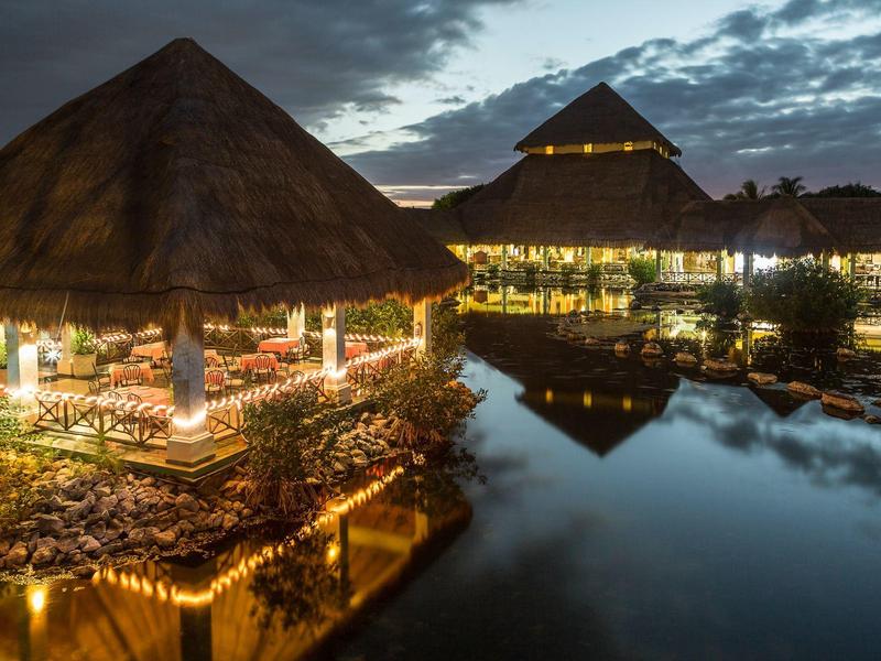 Stimmungsvolle beleuchtete Hütten über Wasser bei Abenddämmerung mit Wolken am Himmel.