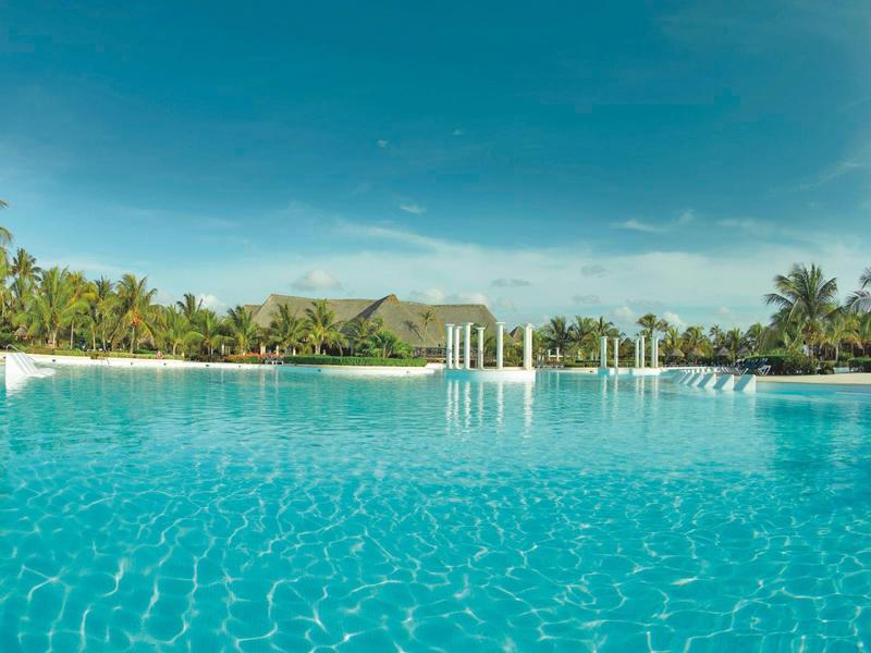 Klare blaue Lagune mit Pavillons und tropischer Vegetation im Hintergrund.
