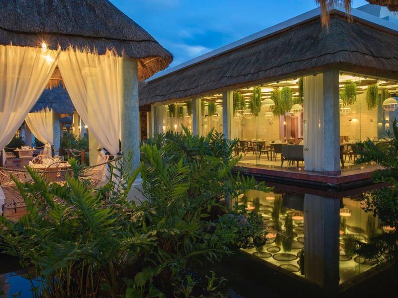 Abendstimmung in einem exotischen Restaurant mit Strohdächern und Wasserbecken.
