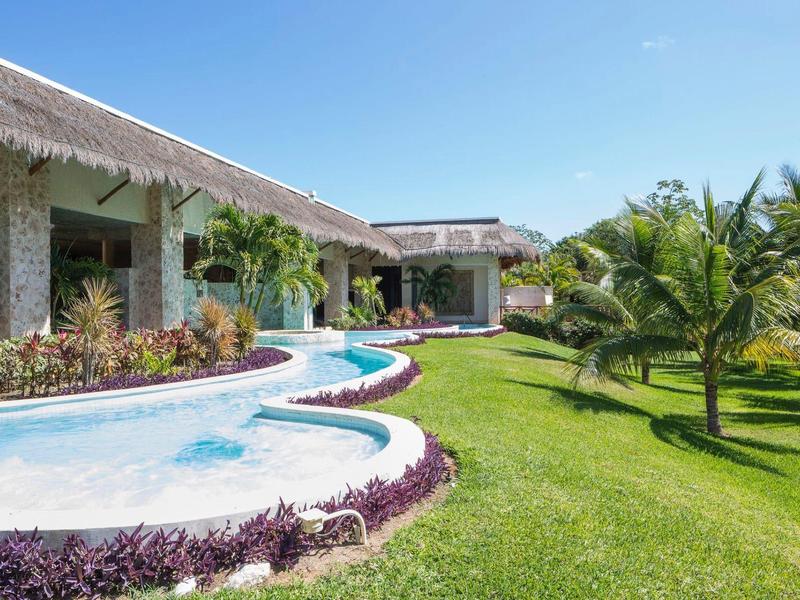 Hotel mit Pool und gepflegtem Garten unter blauem Himmel.