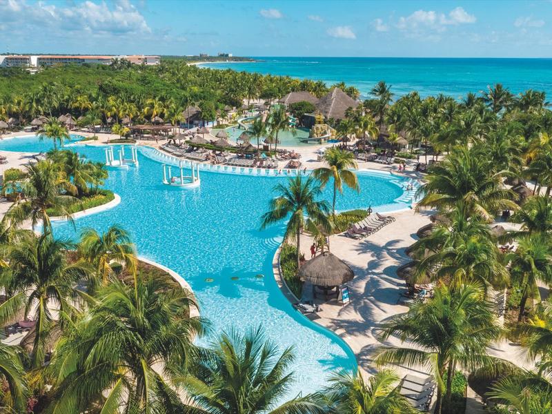 Großer tropischer Pool umgeben von Palmen in einem Hotelresort am Meer.