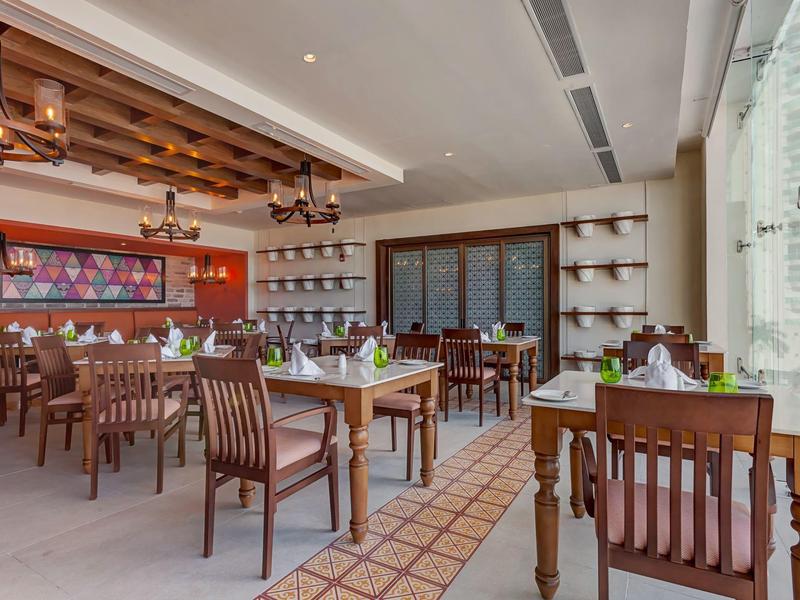 Modernes Restaurant mit Holztischen und -stühlen, großen Fenstern und dekorativem Deckenbalken.