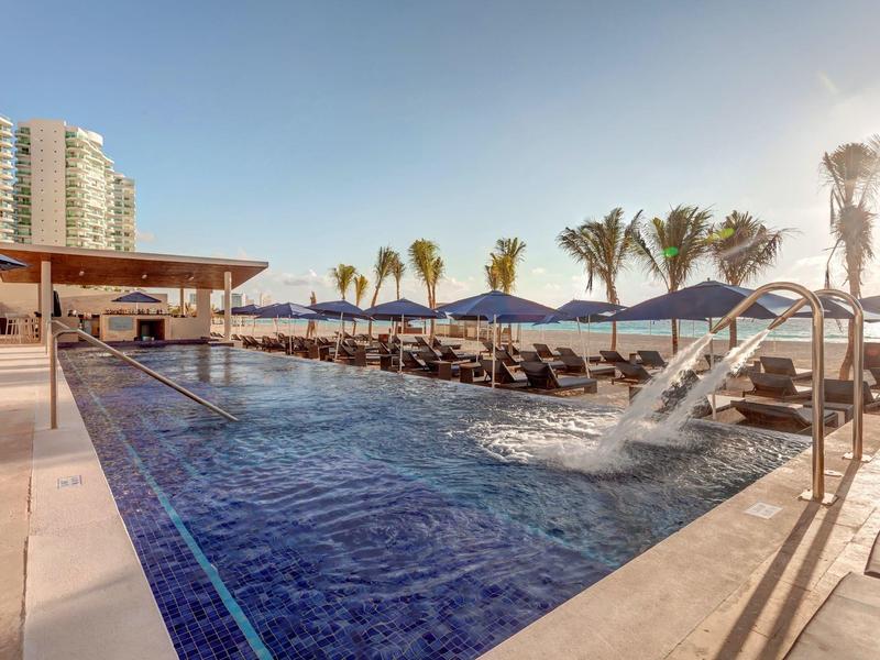 Moderner Außenpool mit blauer Wasserfläche, Liegestühlen und Palmen unter klarem Himmel.