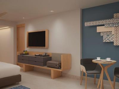 Modernes Schlafzimmer mit weißem Bett, Wand-TV, Holzmöbeln und kleinem Esstisch vor blauer Wand.