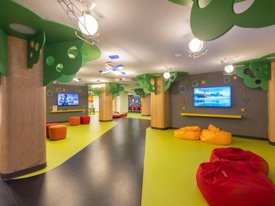 Kinderfreundlicher Raum mit bunten Sitzsäcken, Baumdekor und Bildschirmen an den Wänden.