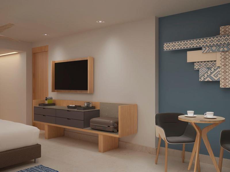 Modernes Schlafzimmer mit weißem Bett, Wand-TV, Holzmöbeln und kleinem Esstisch vor blauer Wand.