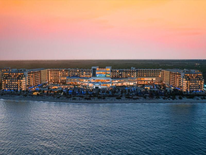 Licht beleuchtete Insel mit Gebäuden und Booten, ruhiges Meer, bunter Sonnenuntergangshimmel.