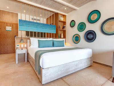 Helles Schlafzimmer mit Doppelbett, Holzregal, blauen Akzentkissen und dekorativen Wandteller in Blau- und Grüntönen.