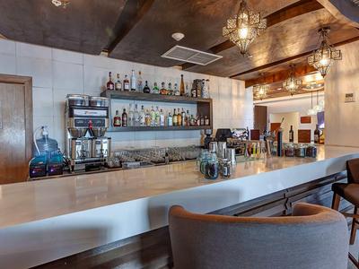 Moderne Bar mit weißer Theke, Holzdecke, eleganten Stühlen und vielfältigen Flaschenregalen.