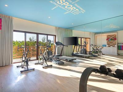 Helles Fitnessstudio mit Cardio-Geräten und großen Fenstern mit Blick ins Grüne.