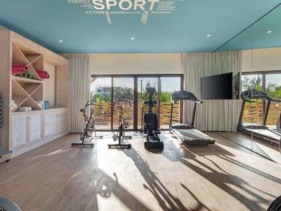 Heller, moderner Fitnessraum mit Trainingsgeräten und großen Fenstern, die Tageslicht hereinlassen.