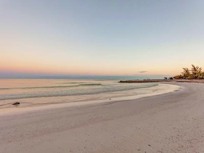 Breiter Sandstrand mit sanften Wellen, weiter Horizont und pastellfarbener Himmel bei Sonnenuntergang.