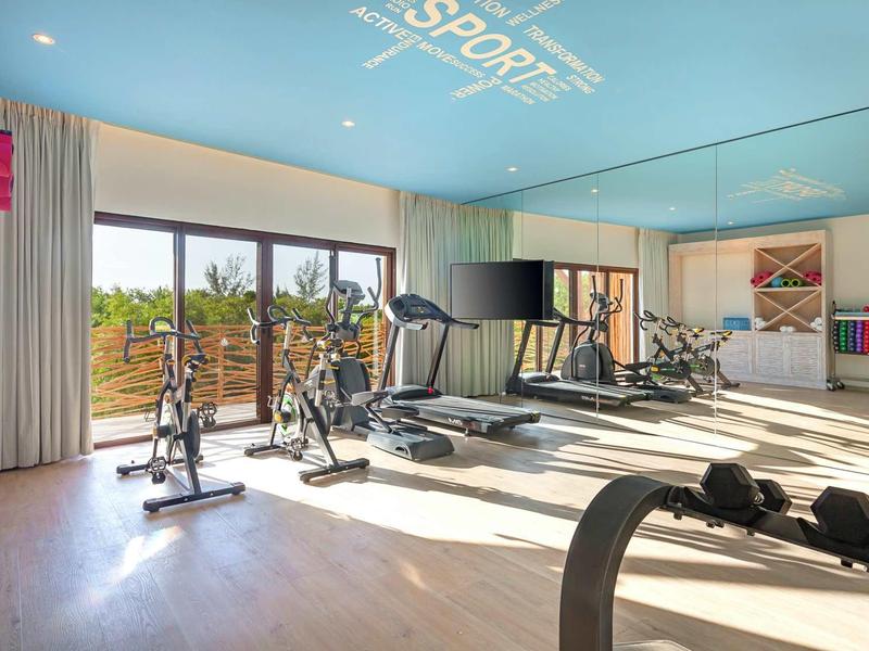 Heller Fitnessraum mit großen Fenstern, mehreren Ergometern, Laufbändern und Spiegelwand.