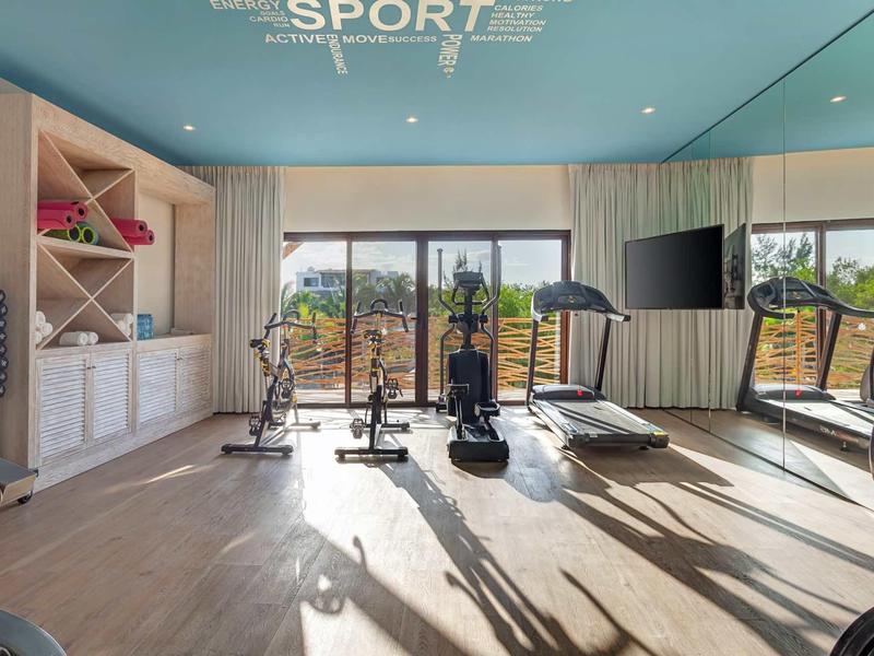 Moderner Fitnessraum mit Sportgeräten, großen Fenstern und hellem Holzboden.