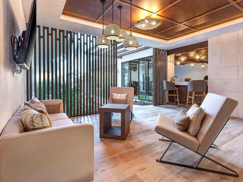 Moderner Wohnbereich mit beiger Couch, zwei Sesseln, Holzboden und stilvollen Deckenleuchten.