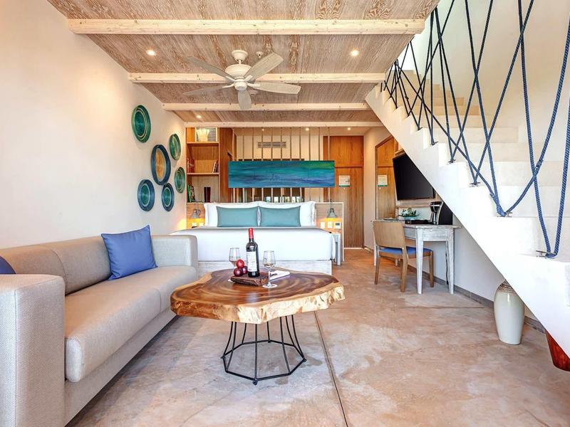 Moderner Wohnraum mit hellgrauer Couch, Baumstamm-Couchtisch, blauen Kissen und Holzdeckenbalken.