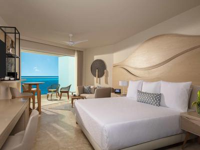 Modern hotel room with sea view, double bed, and balcony seating area.