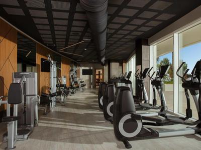 Moderner Fitnessraum mit verschiedenen Trainingsgeräten und großen Fenstern mit Aussicht.