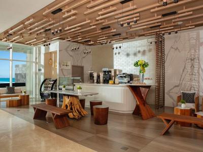 Modern hotel lounge area with sea view, wooden furniture, and sculptural ceiling.