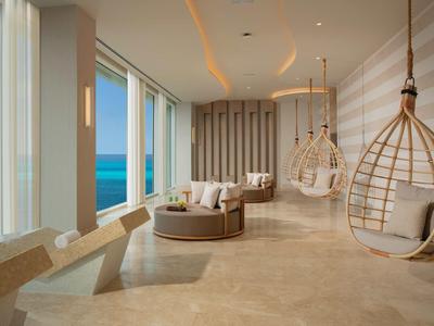 Bright lounge area with large windows overlooking the sea, featuring modern hanging swing chairs.
