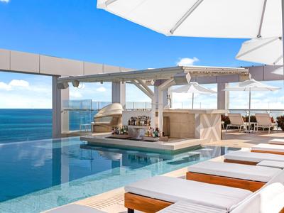 Hotelpool mit Liegestühlen und Meerblick unter klarem Himmel.