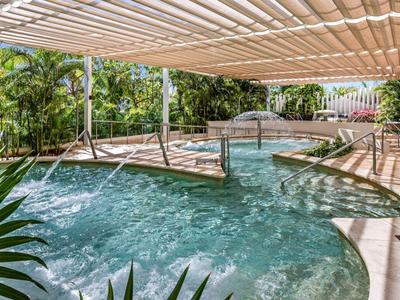 Überdachter Pool mit Wasserspielen und Liegestühlen in einem tropischen Hotelgarten.