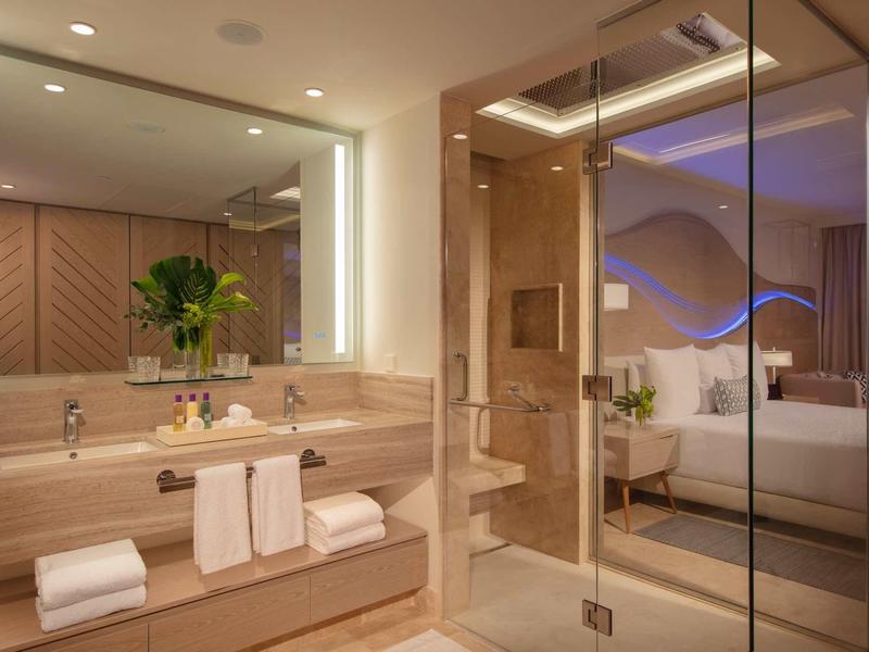 Modern bathroom with large mirrors, wood paneling, and glass door to the bedroom.