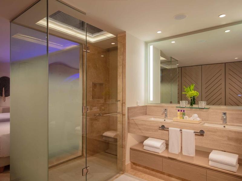 Modern bathroom with glass door, large mirror, wooden shelves, and stylish lighting.
