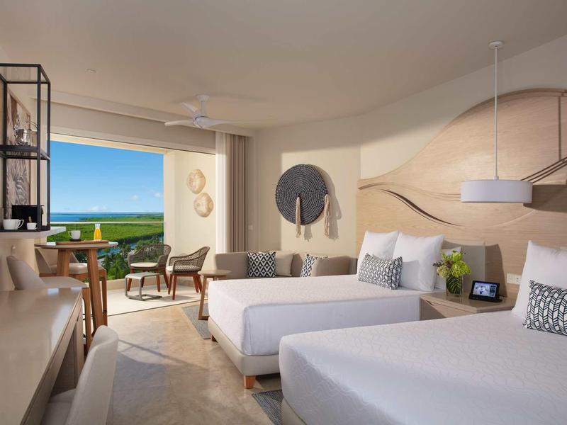 Modern hotel room with two beds, balcony, and sea view.