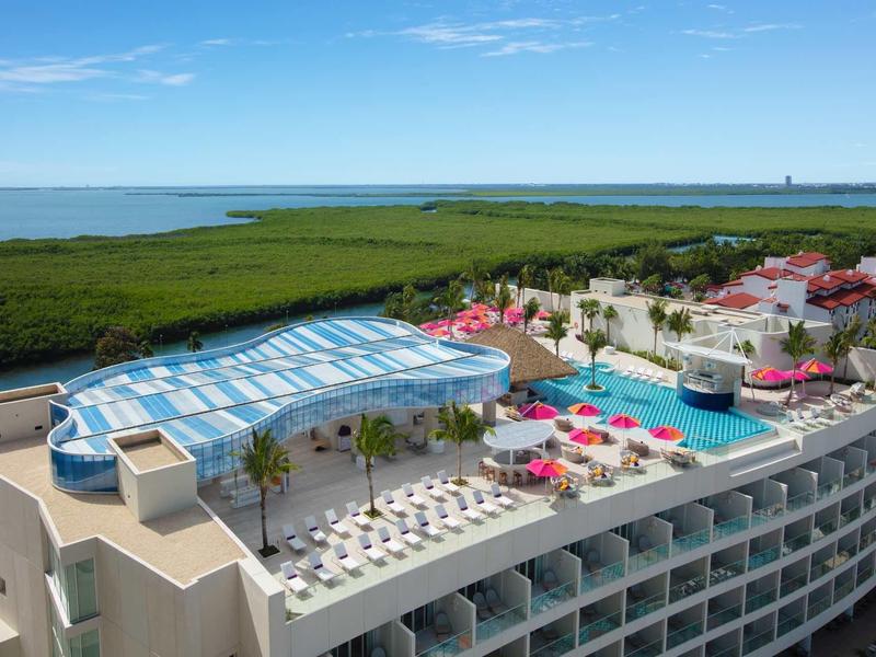 Rooftop pool with glass roof and sun loungers in hotel overlooking green landscape and water.