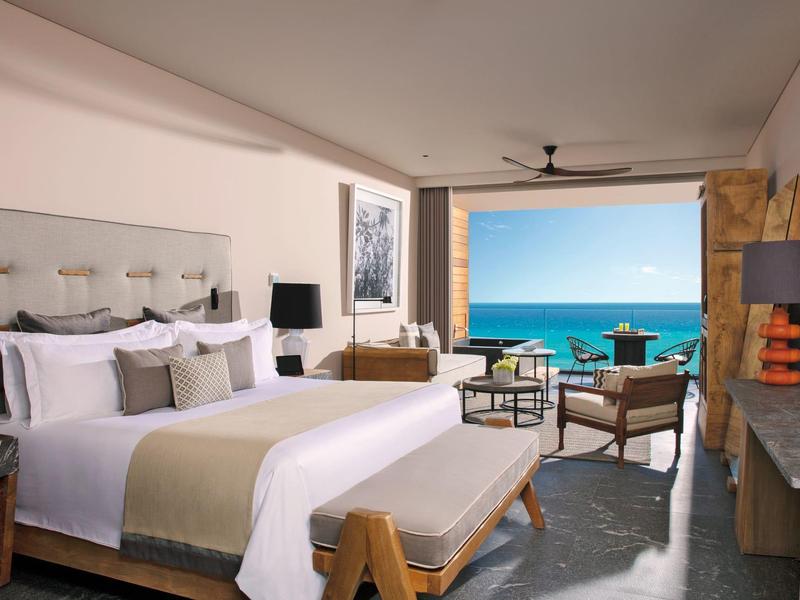 Moderndes Schlafzimmer mit großem Bett, Meerblick, Sitzecke und Kamin in warmen Farben.