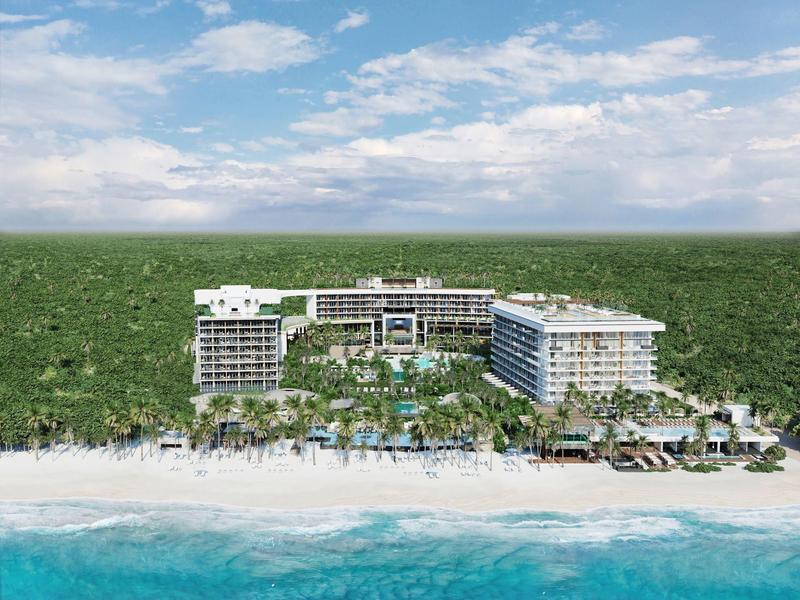 Luxuriöses Hotel am weißen Sandstrand mit türkisblauem Meer und Palmen im Vordergrund.