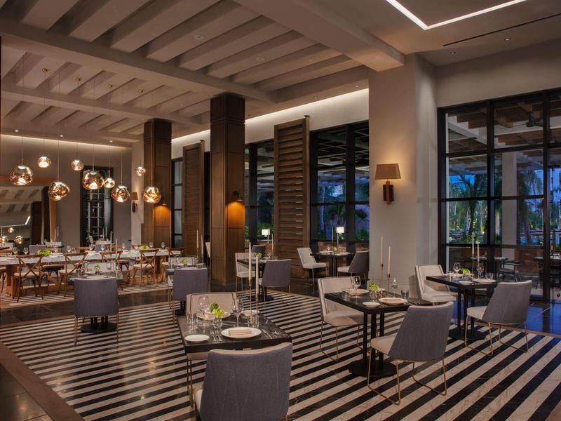 Modernes Restaurant mit schwarzem-weißem Streifenboden, dunkelgrauen Stühlen und warmem Licht.