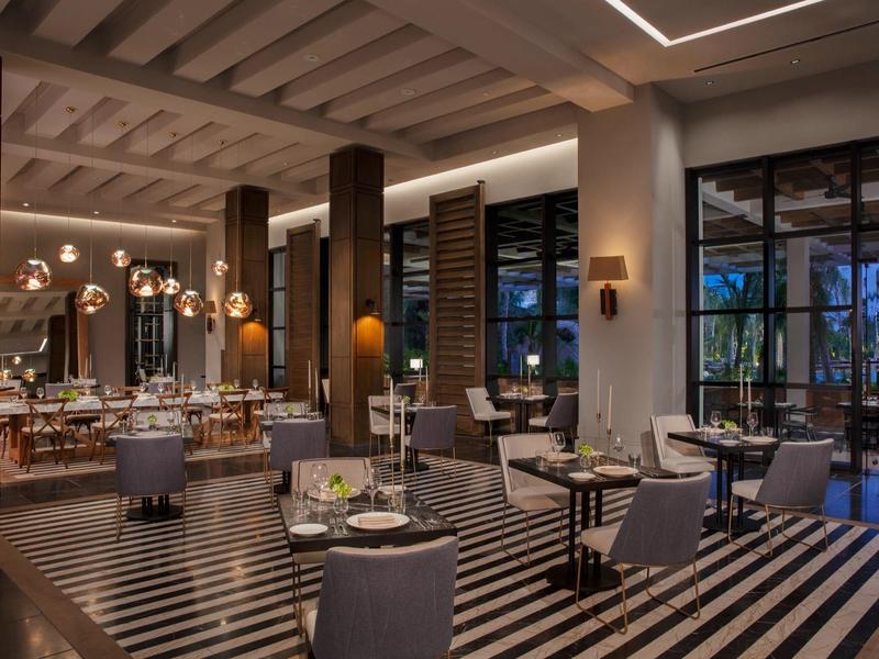 Modernes Restaurant mit gestreiftem Teppich, eleganten Tischen, Holzsäulen und warmem Licht.