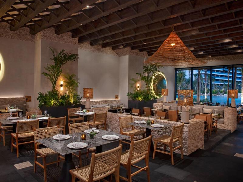 Modernes Restaurant mit Holzbalkendecke, runden Spiegeln, Pflanzen und gedeckten Tischen.