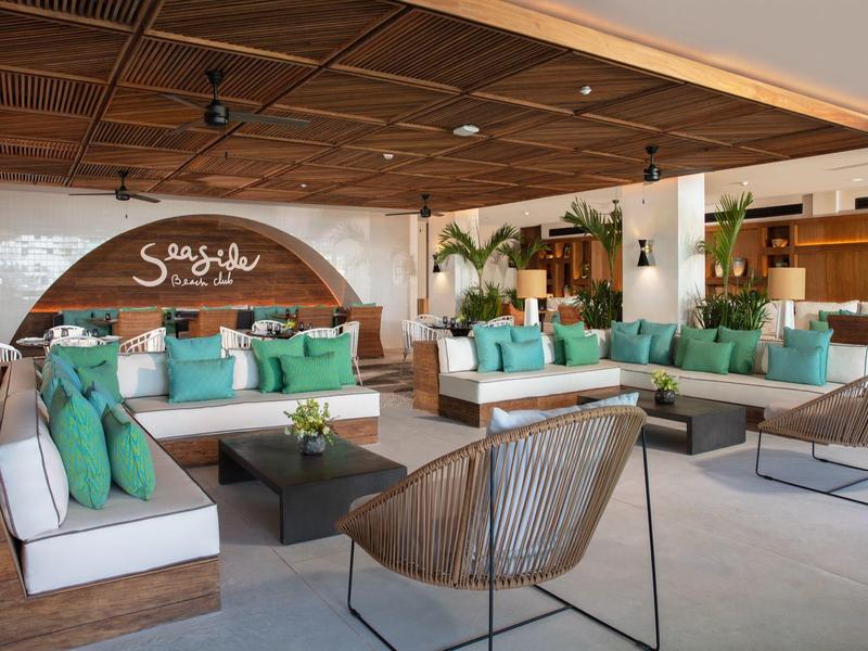 Modernes Lounge-Design mit Holzdach, weißen Sofas, grünen Kissen und Pflanzen in hellem Raum.