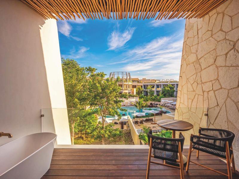 Widok z balkonu z wanną i krzesłami na basen i hotel pod niebieskim niebem.