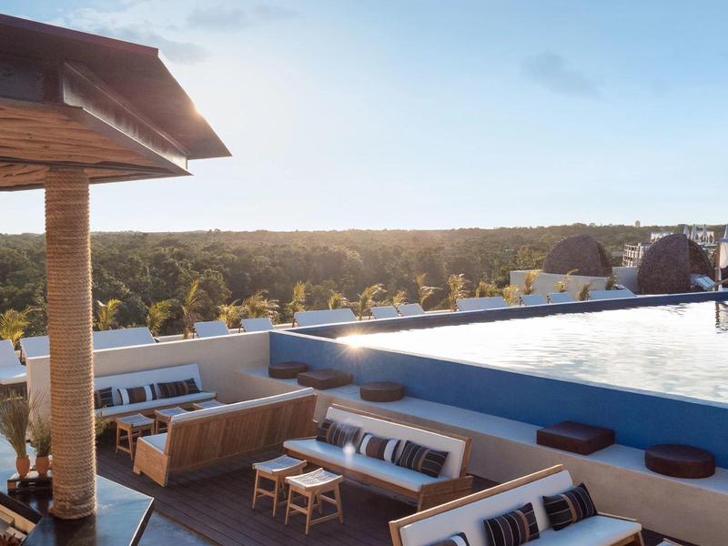 Taras na dachu z basenem infinity, miejscem do siedzenia i widokiem na zielony krajobraz w świetle dziennym.