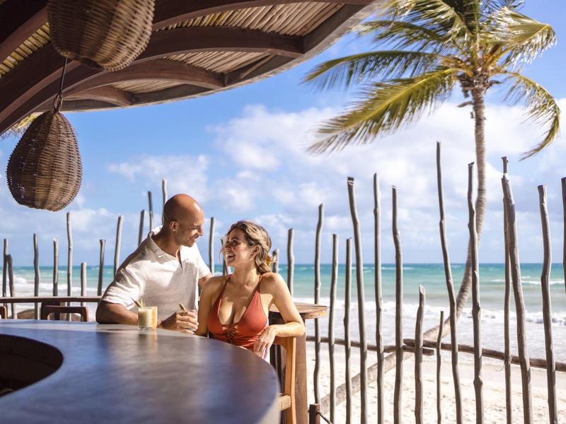 Para delektująca się napojami przy barze na plaży z palmami i widokiem na ocean.