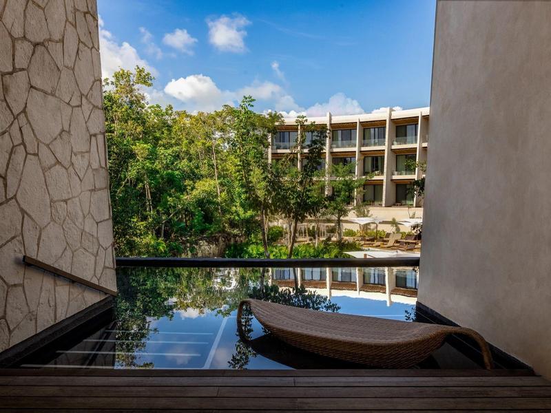 Widok na basen infinity z leżakiem, otoczony naturą i wielopiętrowym hotelem.