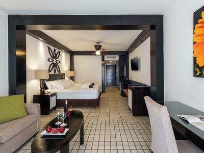 Modern eingerichtetes Hotelzimmer mit großem Bett, Sofa, Tisch und hellen Fliesenboden.