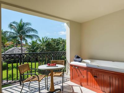 Balkon mit Holztisch, zwei Stühlen, Jacuzzi und Blick auf Palmen und Garten.