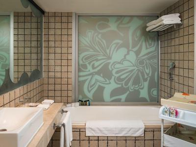 Kleines Badezimmer mit braunen Fliesen, integrierter Badewanne, großer Spiegel und Handtüchern.