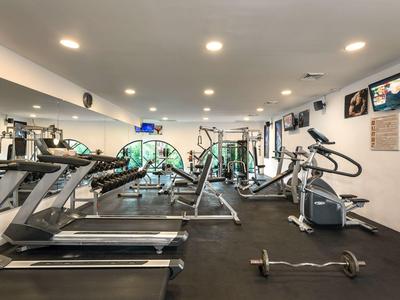 Moderner Fitnessraum mit Laufbändern, Hanteln und Trainingsgeräten in hellem Raum.