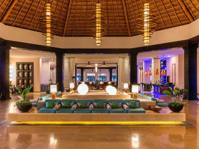 Großer, heller Lobbybereich mit Runddach, Sofas, Pflanzen und moderner Beleuchtung in warmen Tönen.