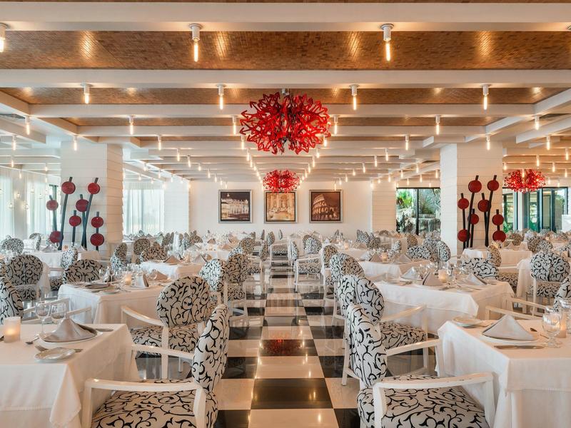 Eleganter Speisesaal mit schwarzen und weißen Fliesen, gedeckten Tischen und roten Dekorationen.