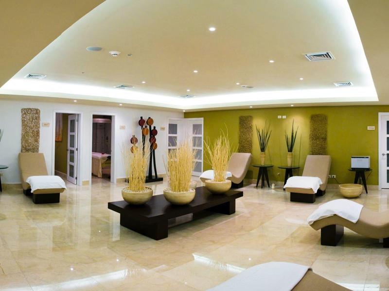 Großer, heller Wellnessraum mit bequemen Liegen, Pflanzen und warmen Grüntönen an den Wänden.