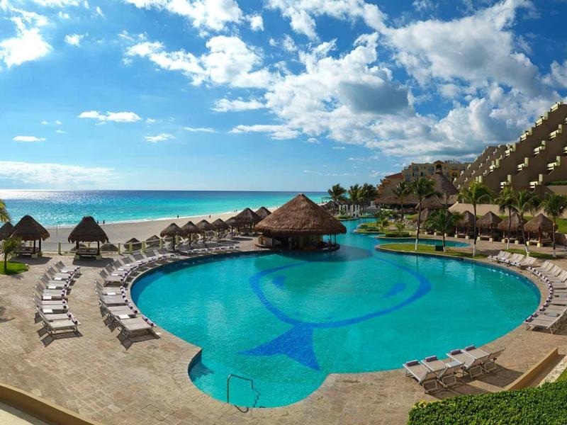Gran piscina del hotel con tumbonas y vista al mar bajo cielo azul.