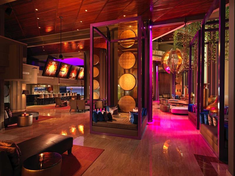 Lobby de hotel con decoración moderna, luz cálida, suelo de madera y áreas de asiento acogedoras.